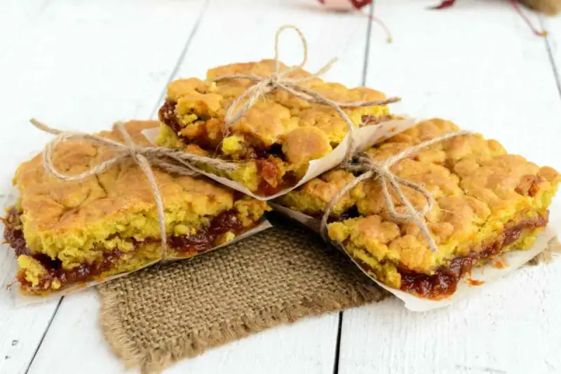 Tre deliziose fette di torta con marmellata, legate con spago e avvolte in carta da forno, pronte per essere gustate.