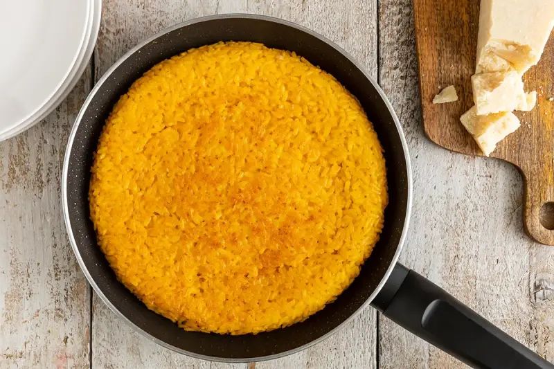 Un invitante riso al salto dorato in padella, pronto per essere gustato con scaglie di Parmigiano Reggiano.