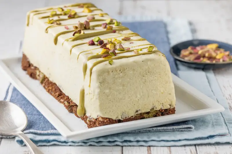 Semifreddo al pistacchio, un dolce gelato decorato con glassa verde e granella di pistacchi, su una base croccante.
