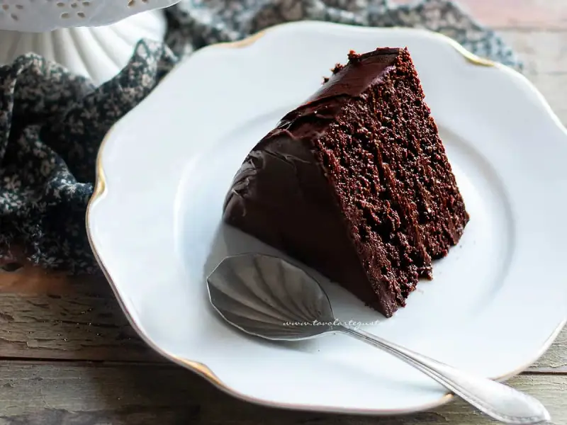 Una fetta di ciambellone al cioccolato, soffice e golosa, su un piatto bianco con un cucchiaino d'argento.