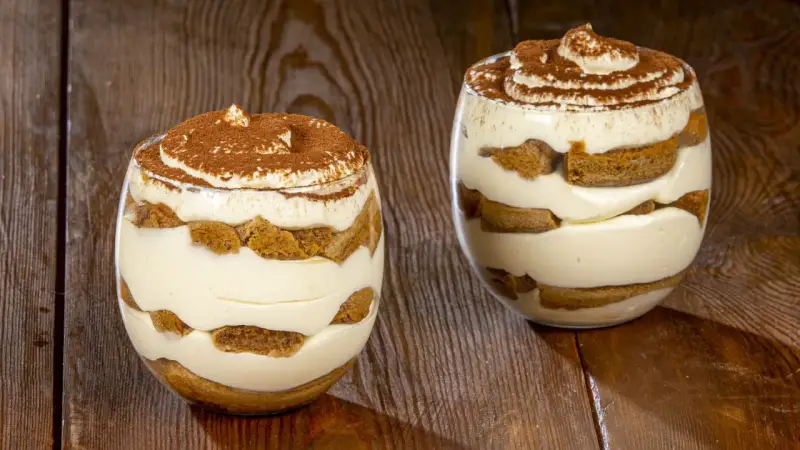 Due bicchieri di delizioso tiramisù senza uova, con strati di savoiardi e crema, spolverati di cacao.